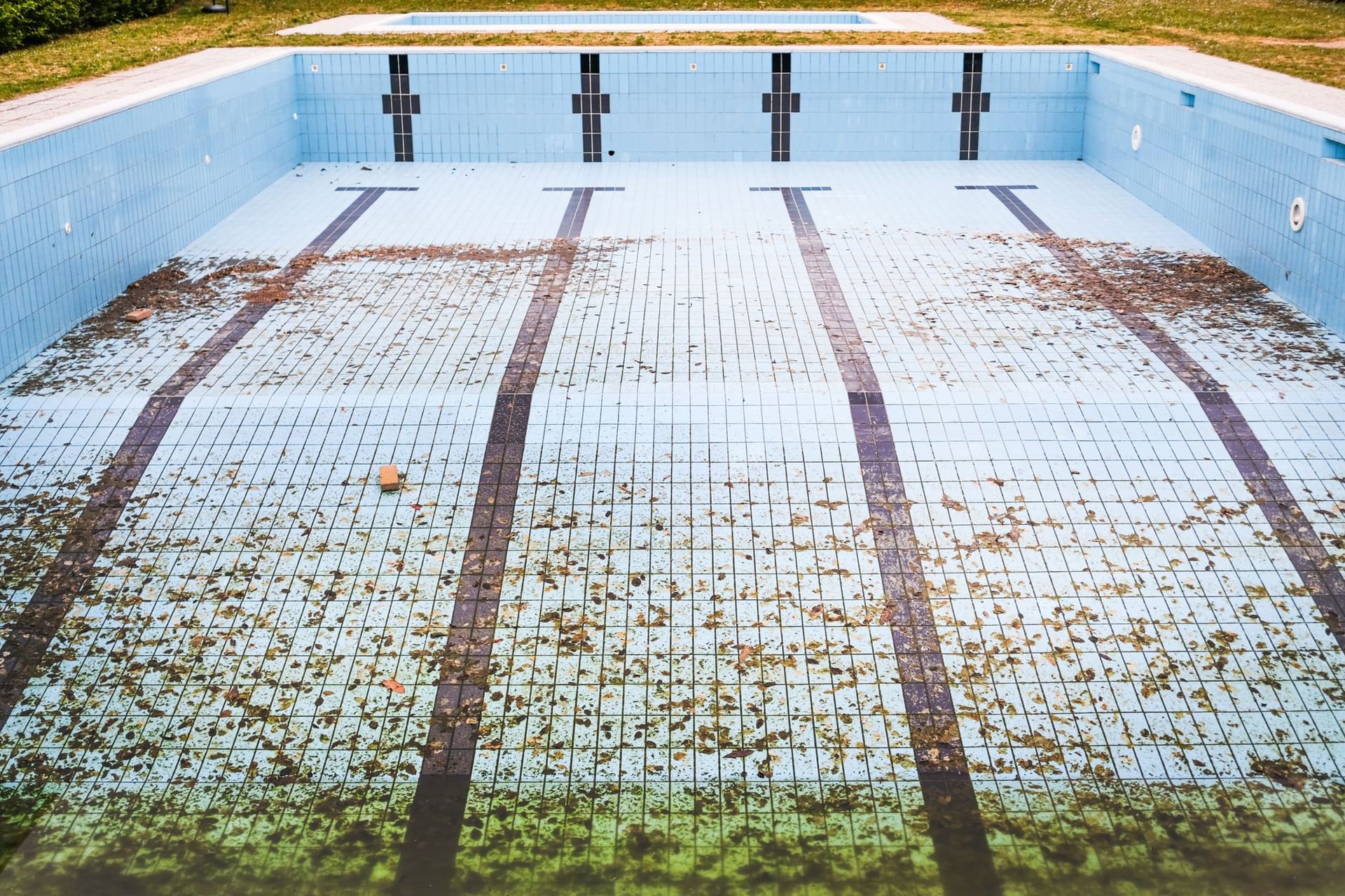 A drained tiled pool with leaves and debris scattered across the floor