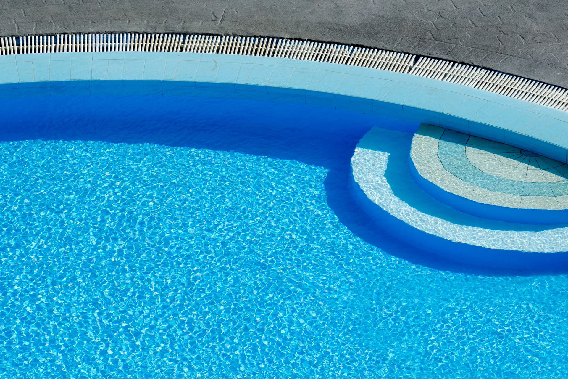 Bright blue pool with a curved vinyl-style wall and a built-in step, seen from above in sunlight