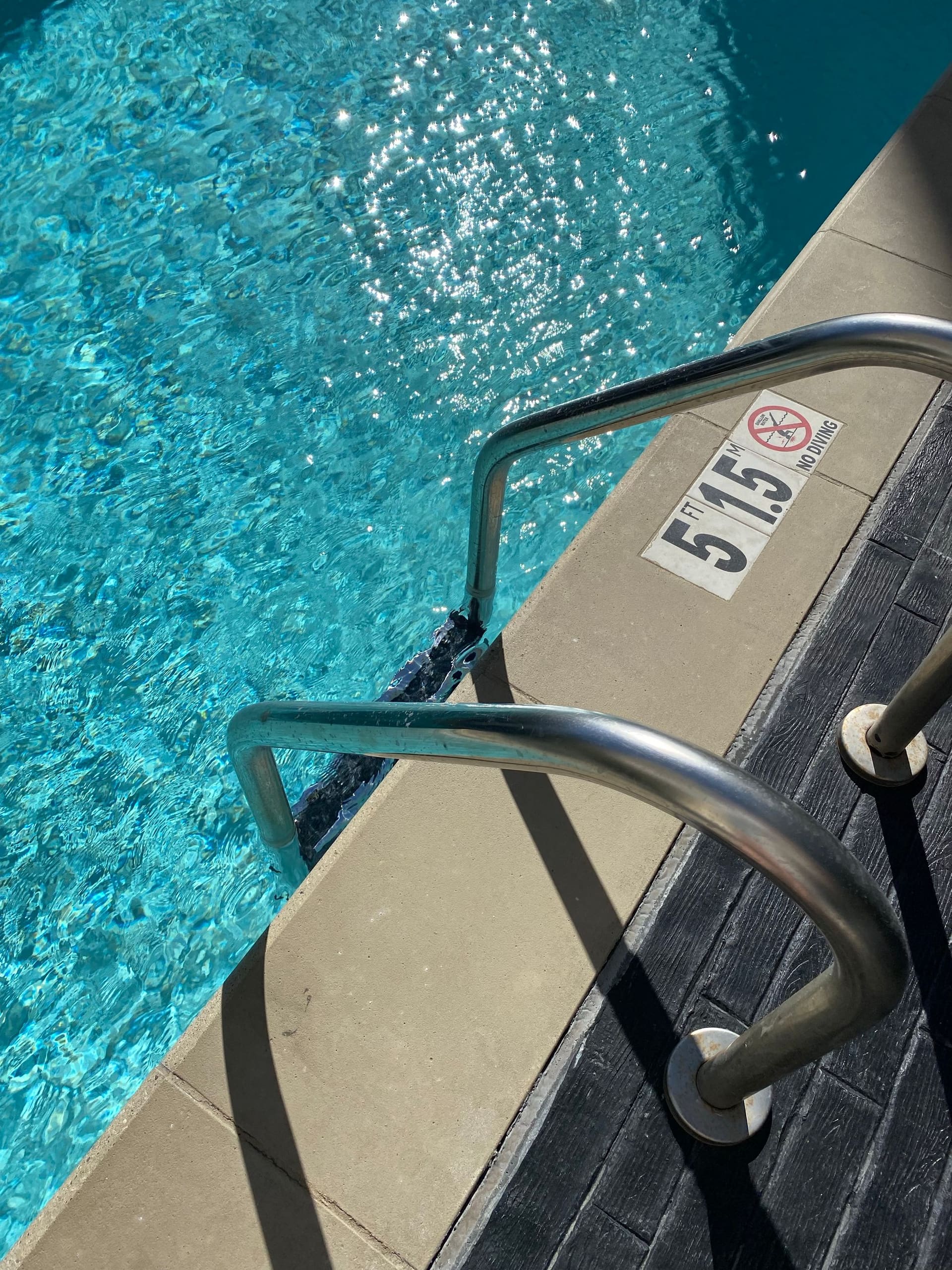 Stainless steel pool ladder beside sunlit blue water