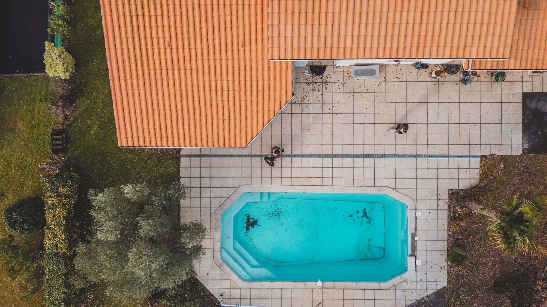 Bird’s-eye view of a small backyard pool beside a house with a tiled patio
